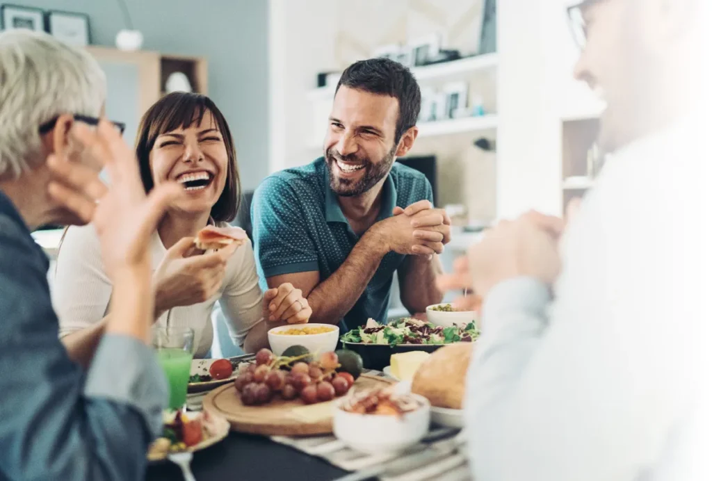 Adults sitting around a modern home smiling and laughing with various greens and fruit on the table
