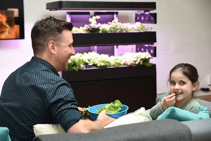 Father sitting on couch with daughter eating lettuce from a bowl with a Terrace Pro 2-Tier in the background