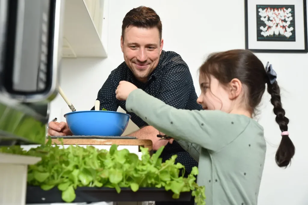 Father with young daughter using leafy greens to make a salad in their kitchen