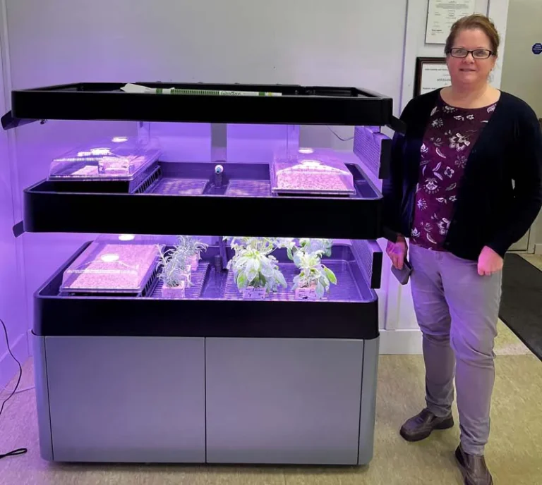 Woman standing next to a 2-Tier Terrace Pro with plants and growing trays inside.