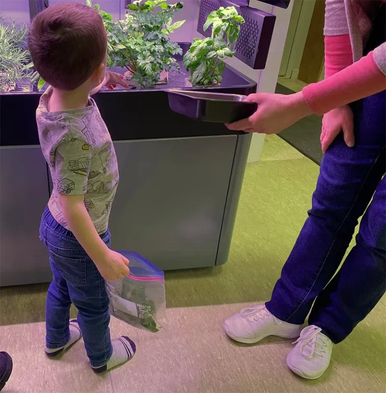 Young child standing in front of Terrace Pro indoor garden with caregiver holding tray