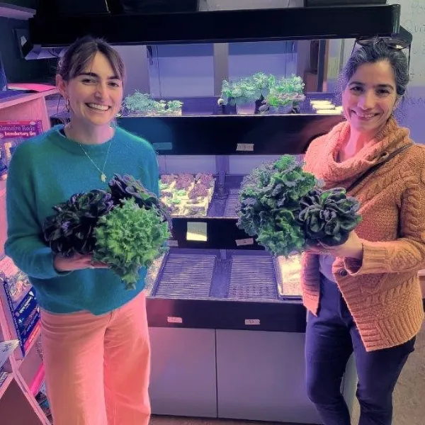 Two women in front of a Terrace Pro holding bunches of lettuce/herbs
